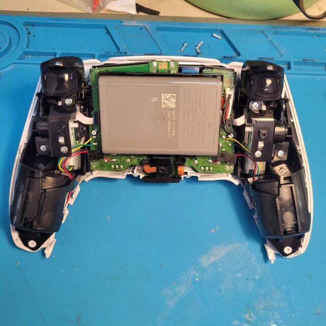 Otwarty pad PlayStation na niebieskiej macie: bateria, płytka i gałki analogowe